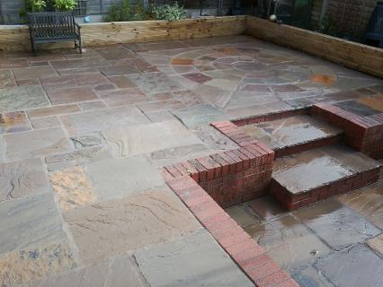 Bueatiful raj green stone patio and steps with wooden decking planter.