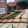 Sleepers, artificial turf and slabbing with stoned areas in front garden.